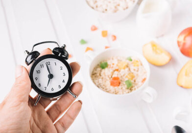 A person's hand holding alarm clock in hand over the breakfast on the table. intermittent fasting